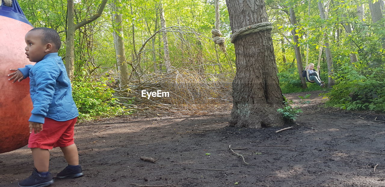 FULL LENGTH OF MAN STANDING BY TREE TRUNK IN FOREST