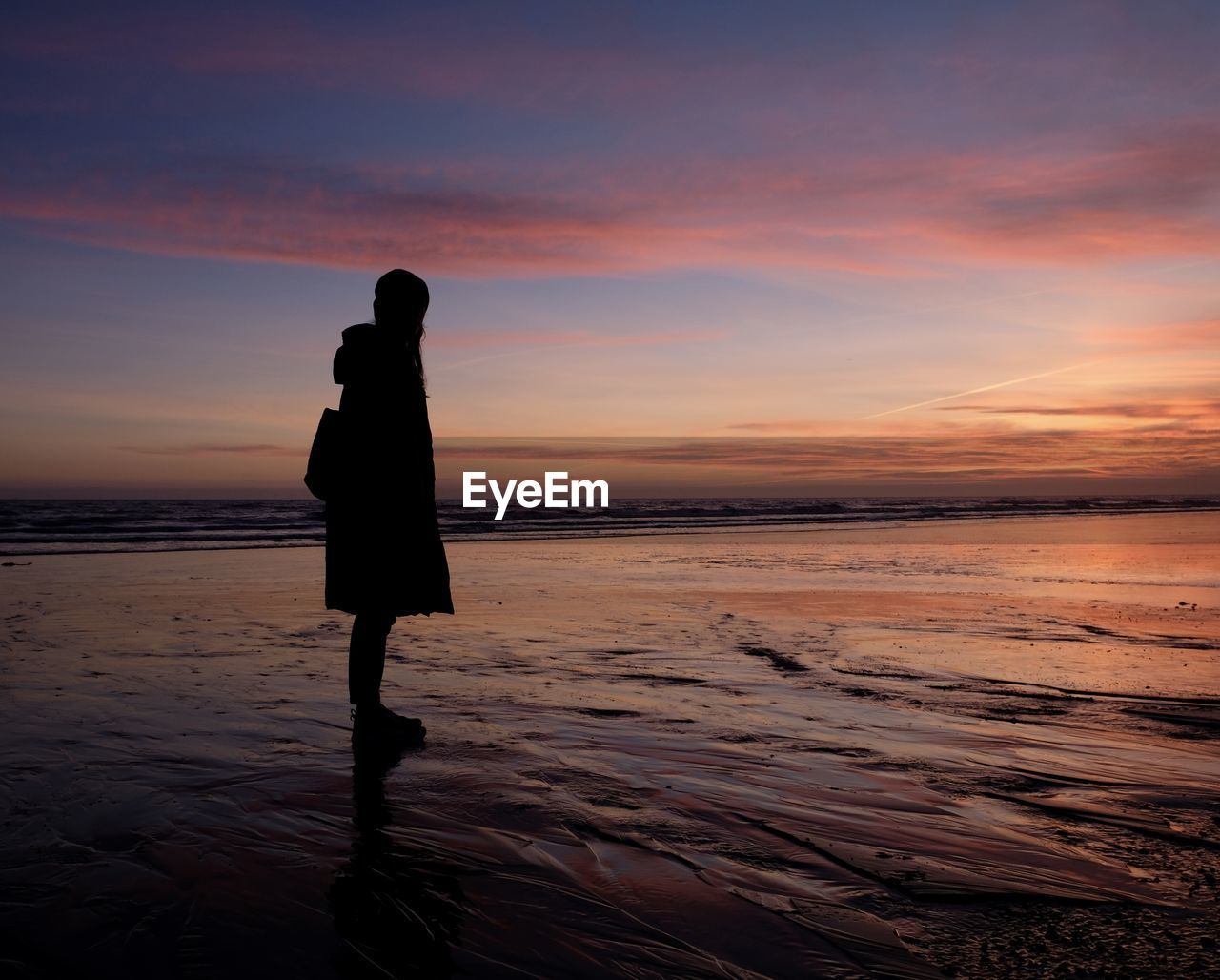 Silhouette woman standing at beach against sky during sunset reflection