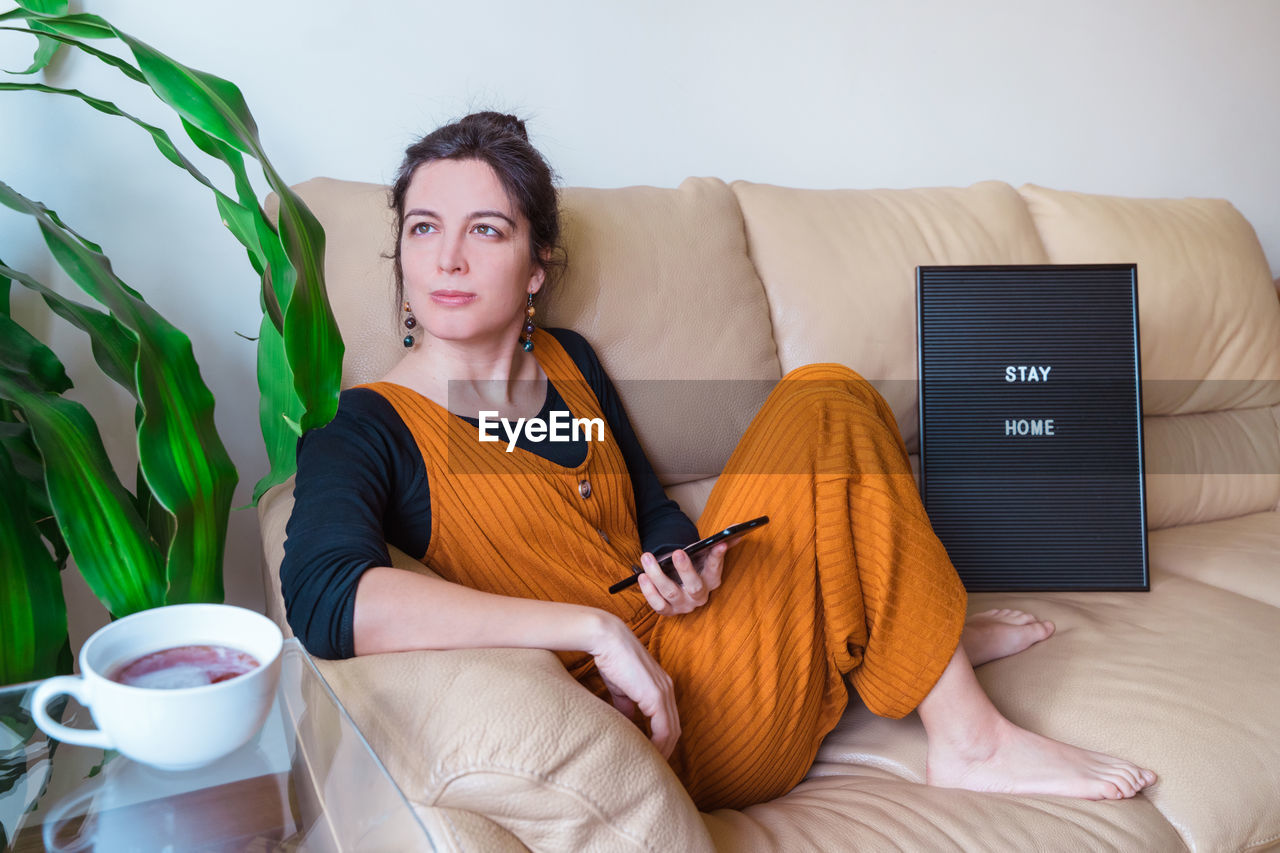 Woman with phone sitting on sofa at home