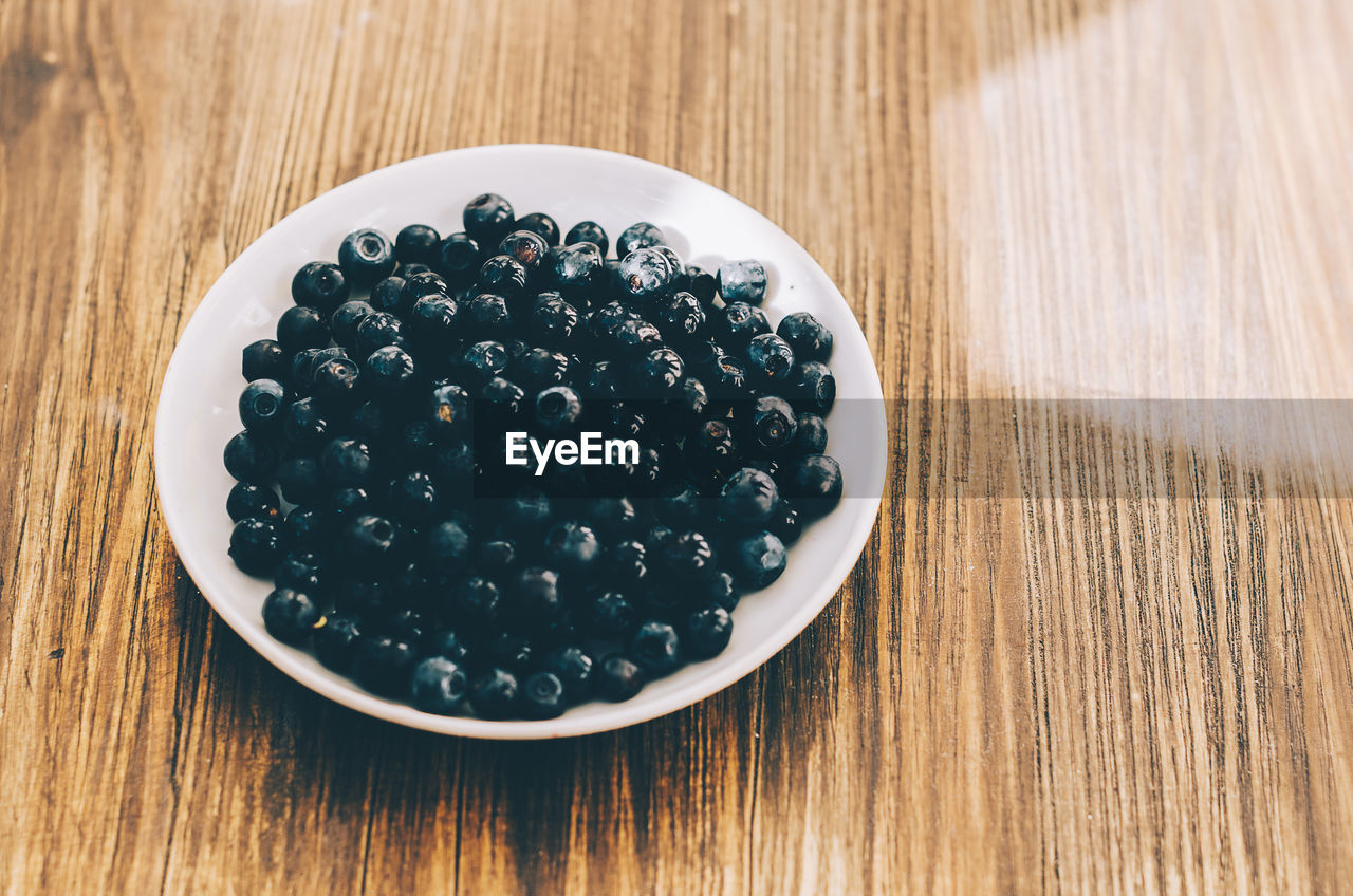 High angle view of blueberries in plate on wooden table