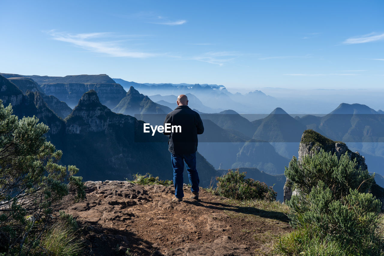 MAN STANDING ON MOUNTAINS AGAINST SKY