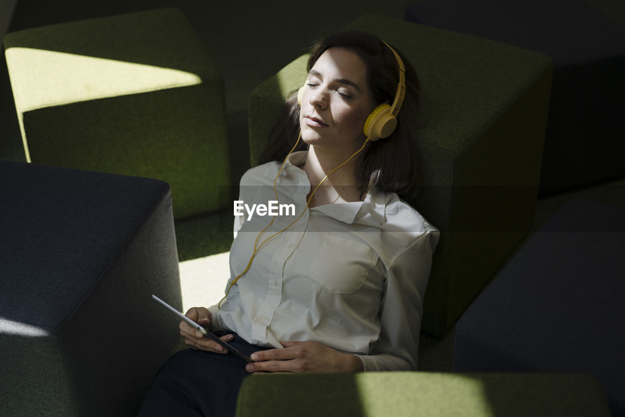 Woman with headphones relaxing while leaning on hassock in office