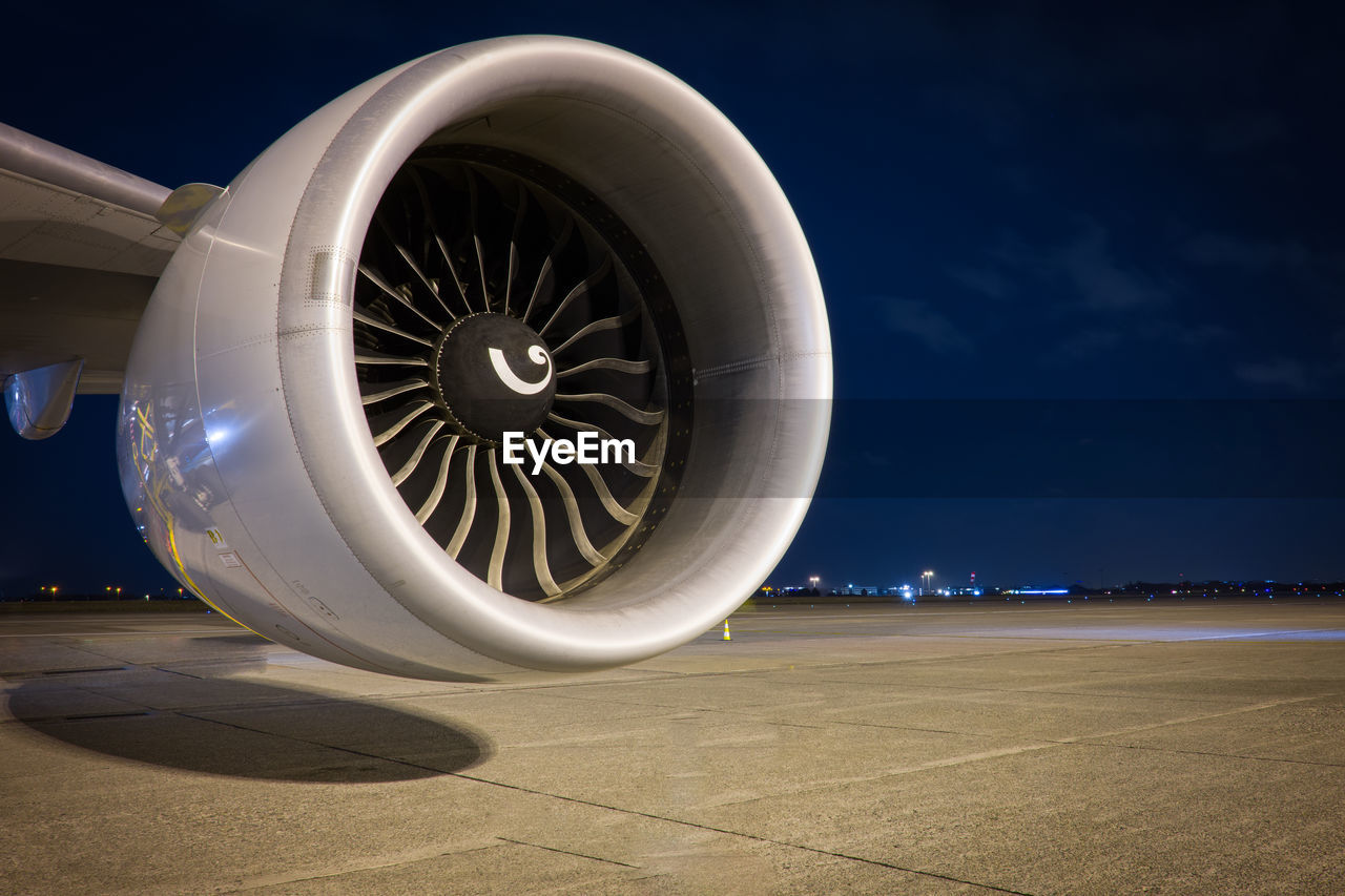 Close-up of jet engine on runway against blue sky