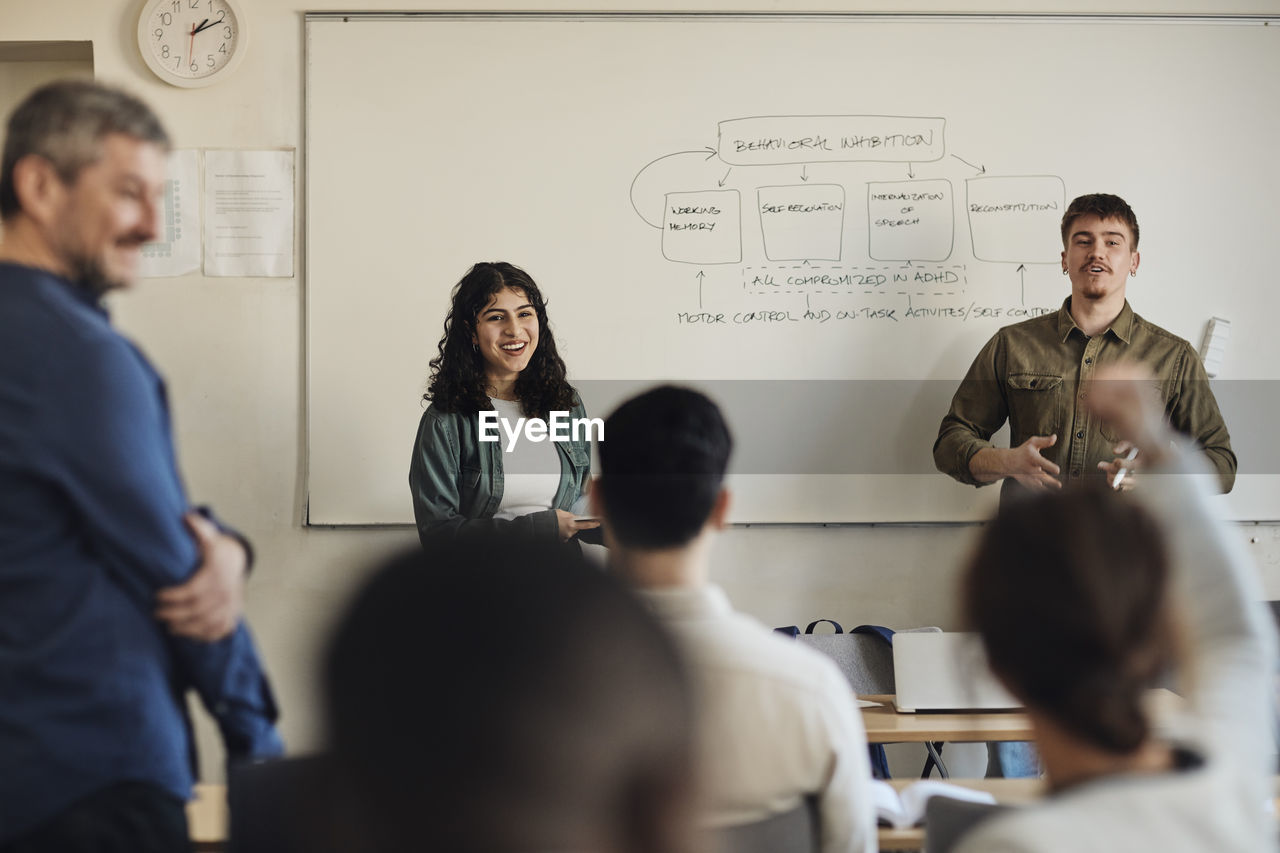 Male and female students interacting with friends during q and a session in classroom