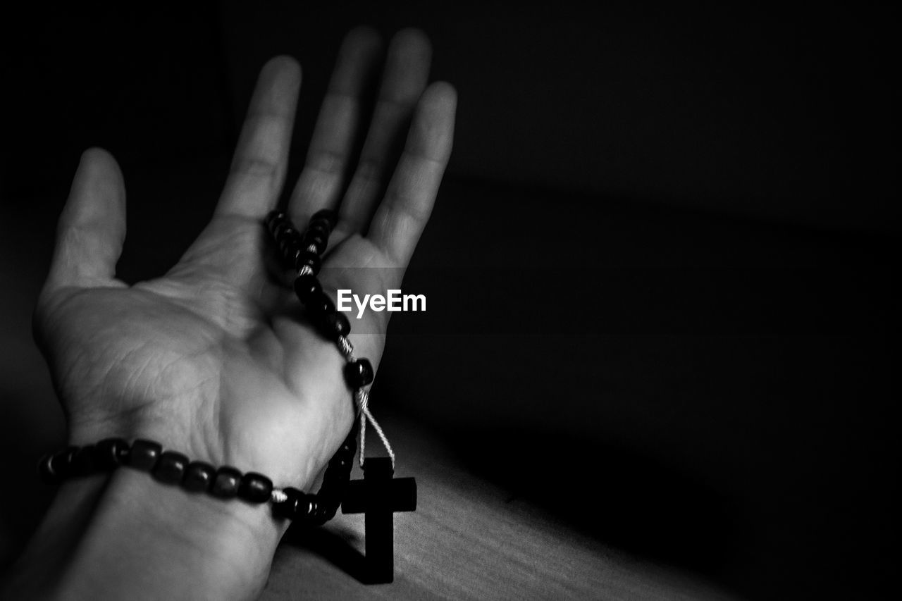 Cropped hand holding rosary on wooden table in darkroom