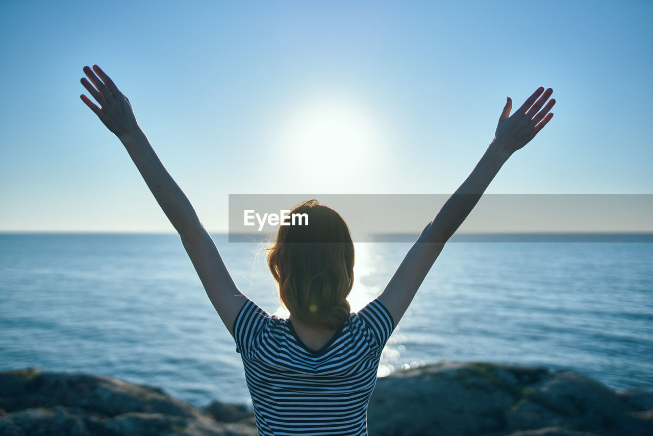 Rear view of woman standing in sea against sky