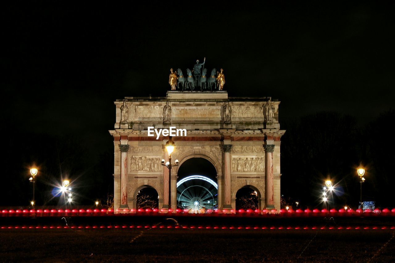 Illuminated street by arc de triomphe du carrousel against sky at night