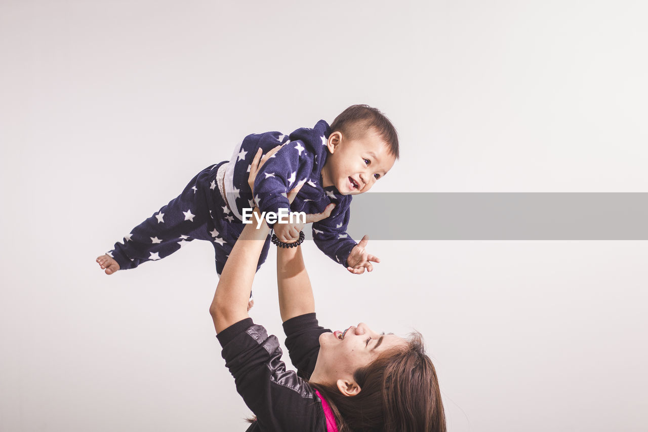 Smiling mother carrying son against white background