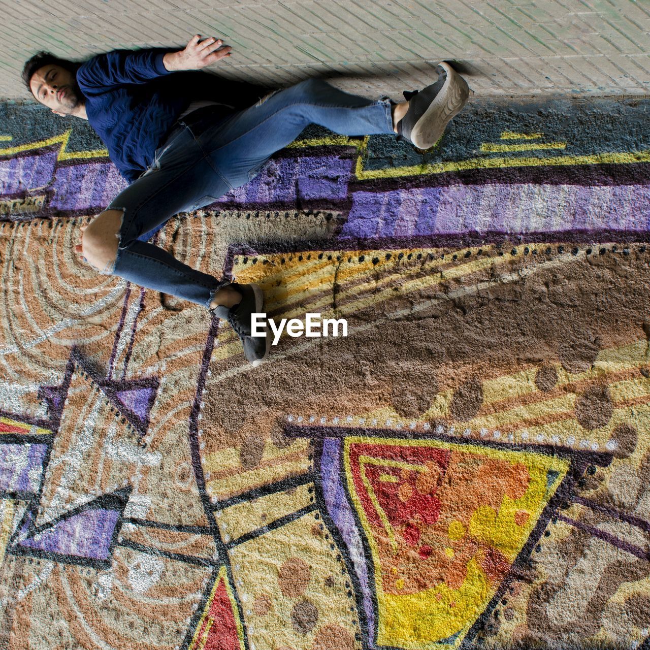 Upside down image of man lying on footpath by wall with graffiti