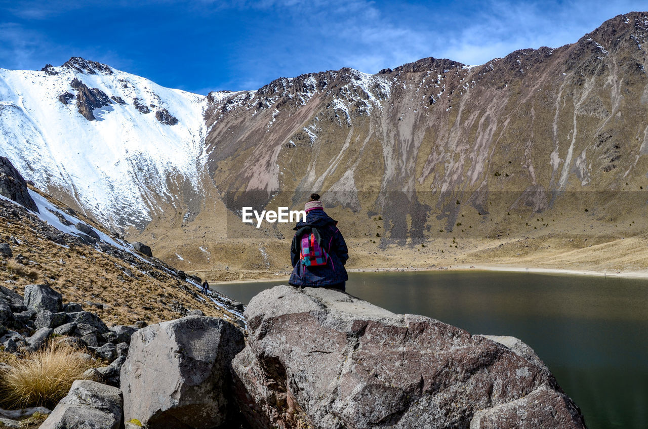 Rear view of woman sitting on rock against mountains