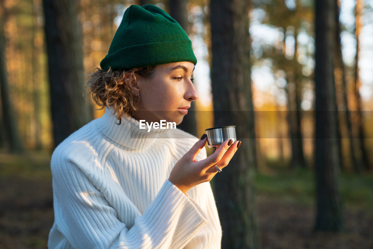 Young woman drink hot tea or coffee from thermos cup walk in autumn forest enjoy nature outside city