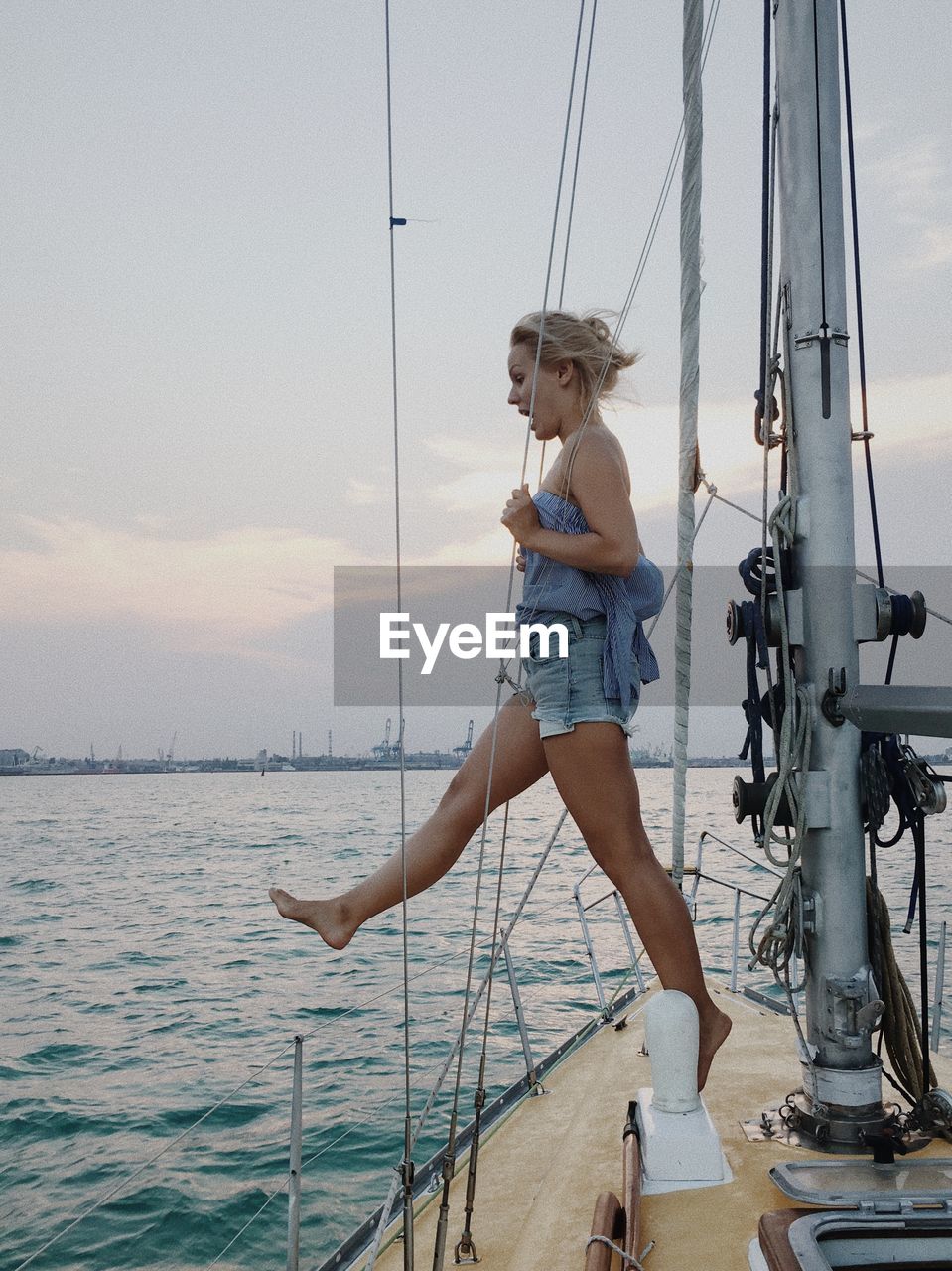 Young woman standing in sailboat against sky