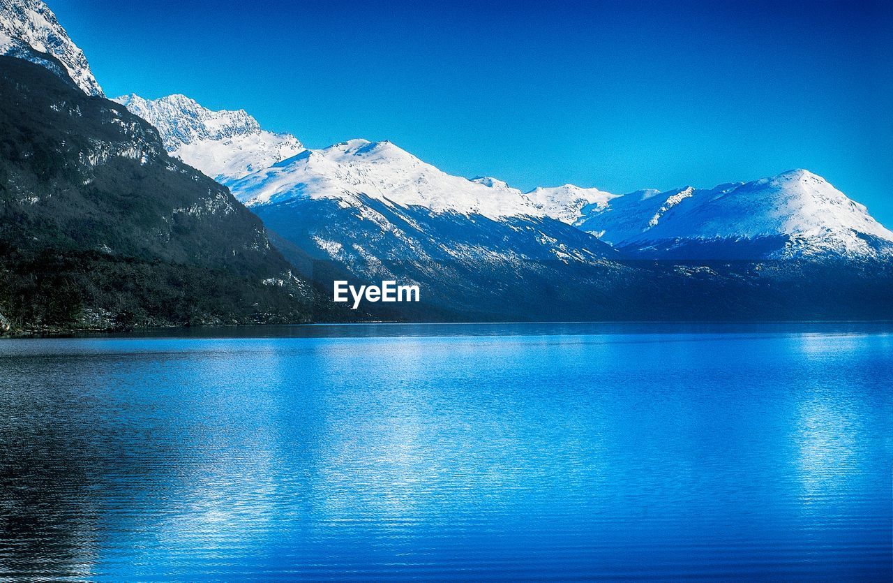 Scenic view of lake and snowcapped mountains against blue sky