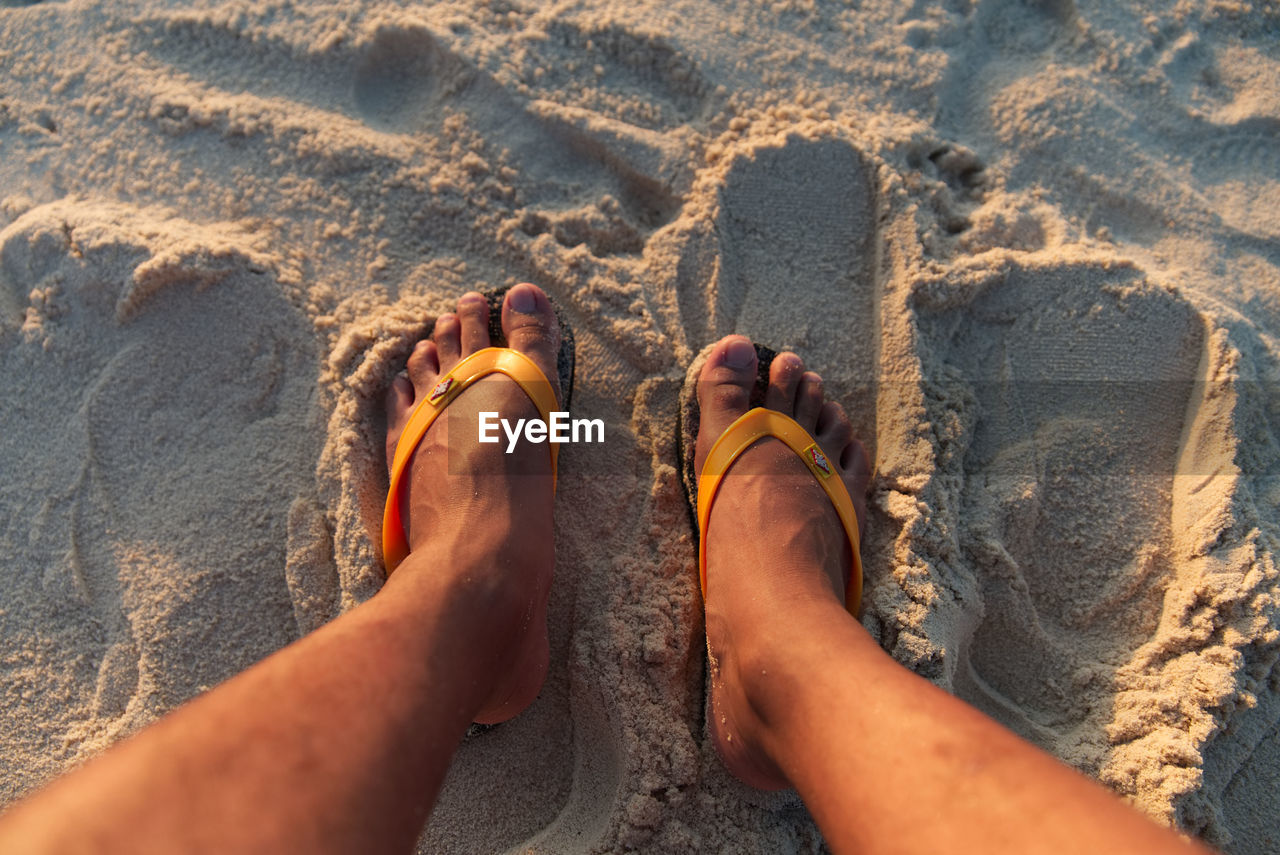 Low section of man wearing slippers on sand at beach