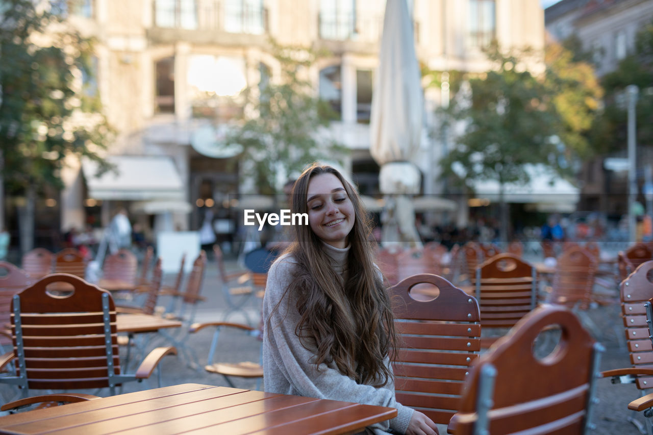 Smiling young woman sitting on seat in city