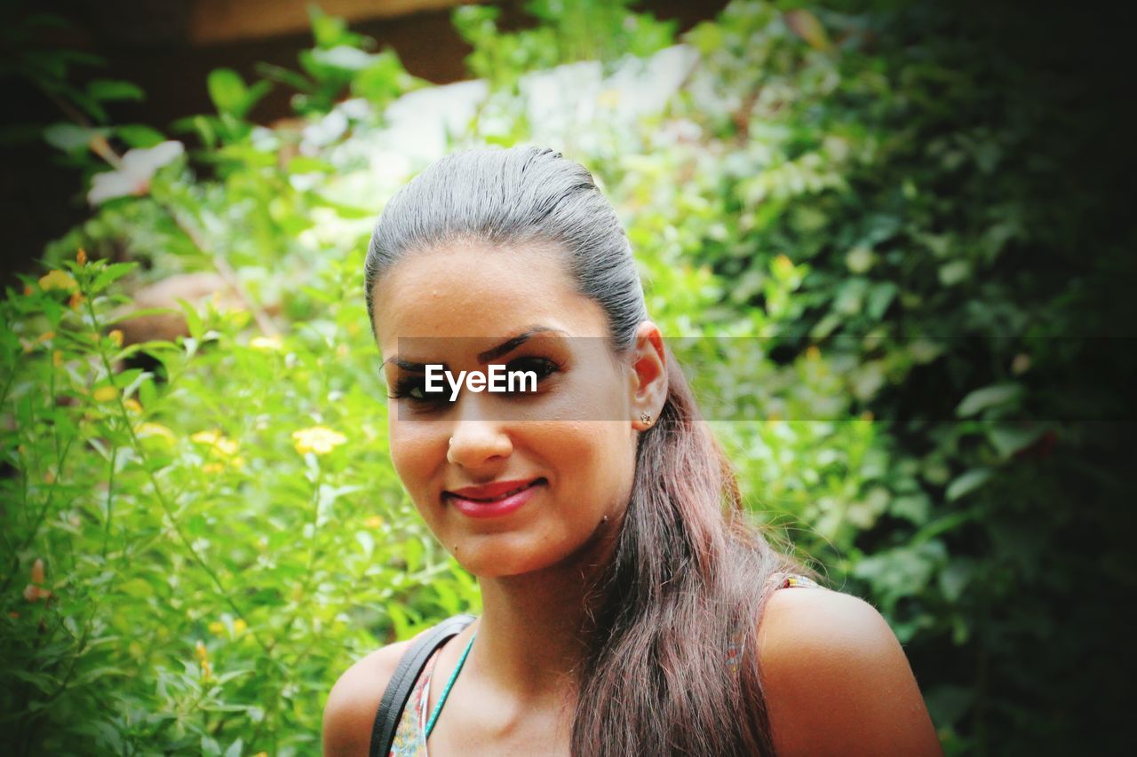 Close-up portrait of beautiful woman against plants at park