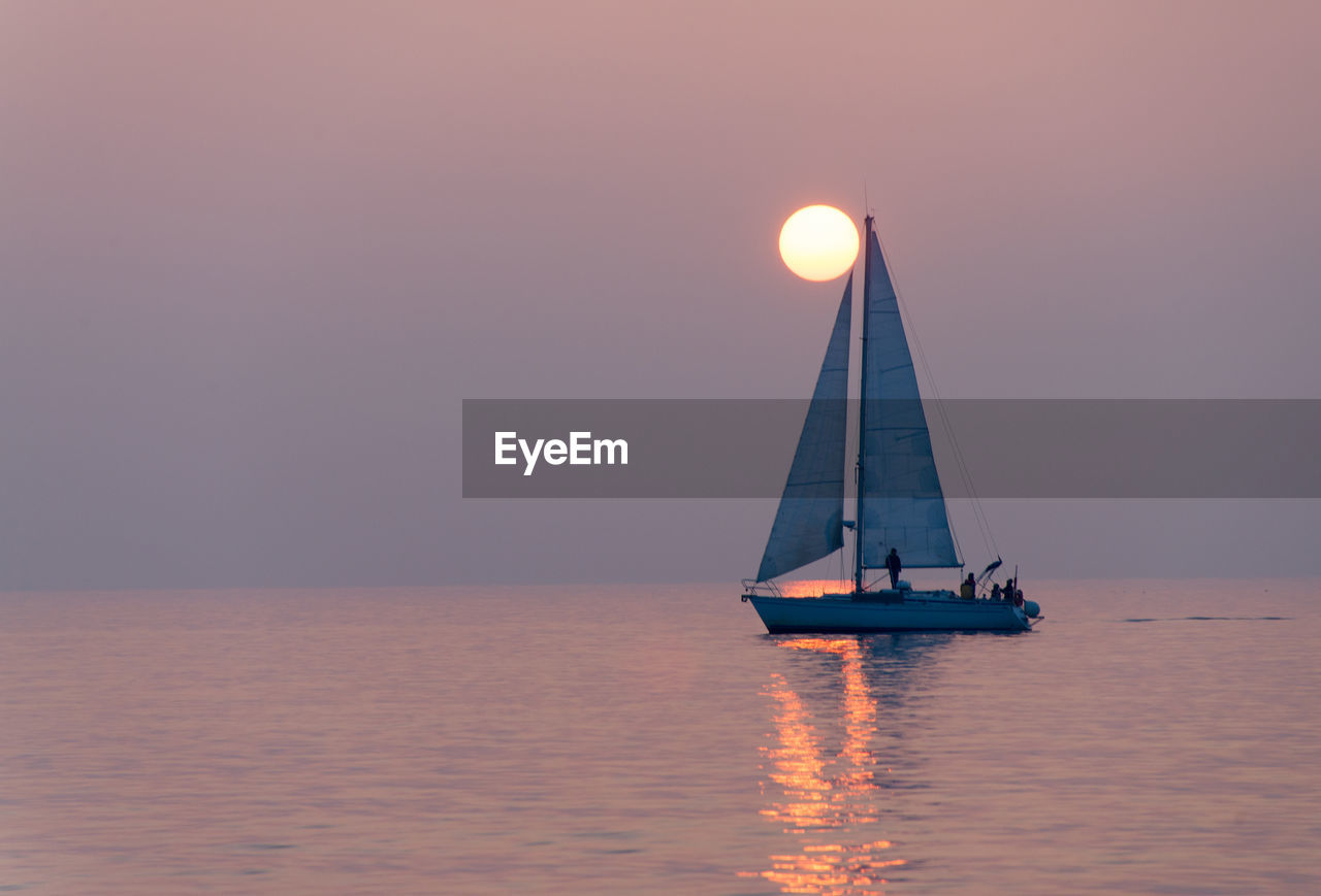 Sailboat sailing on sea against sky during sunset