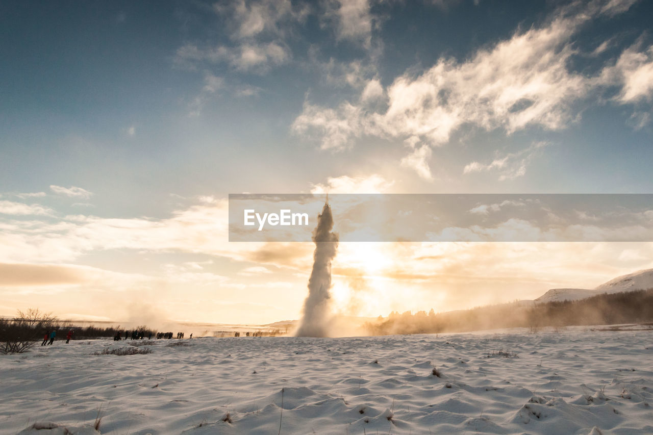 Geyser on snow covered landscape against sky during sunset