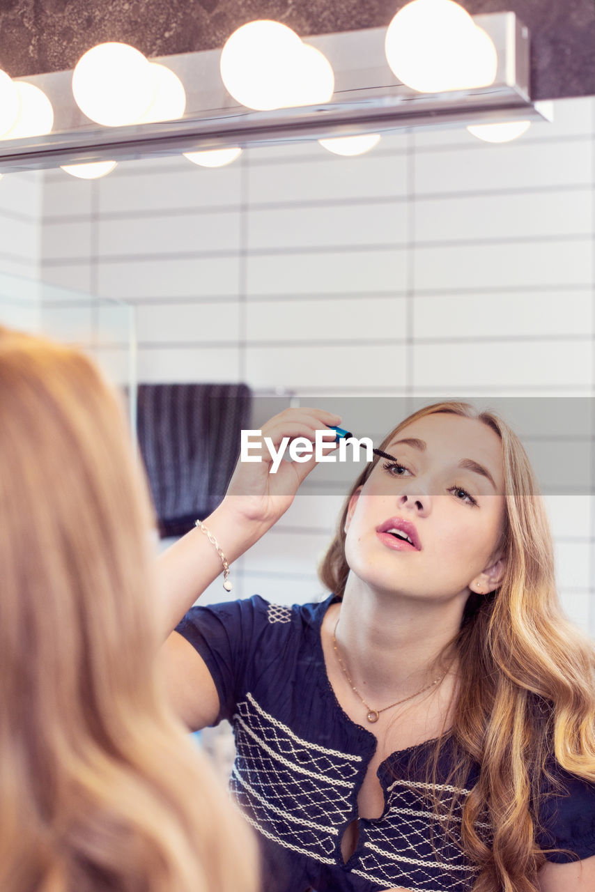 Young woman applying mascara in front of bathroom mirror