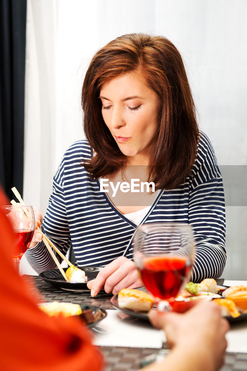 Beautiful woman eating food with friend in foreground sitting at restaurant