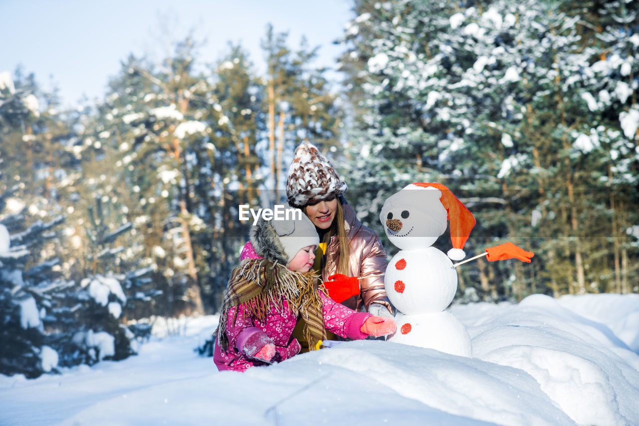 Cheerful mother and daughter making snowman during winter