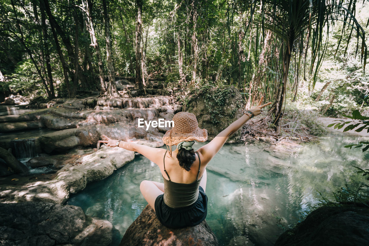 Rear view of woman standing by pond in forest