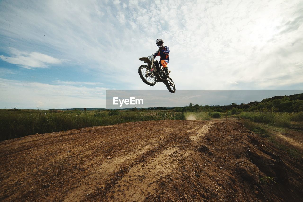 Man with motorcycle jumping on landscape against sky