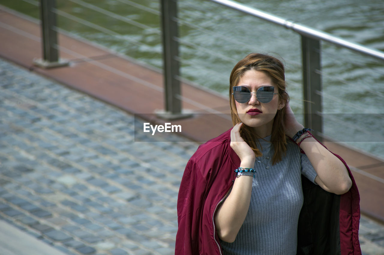 Smiling woman looking away while standing against railing