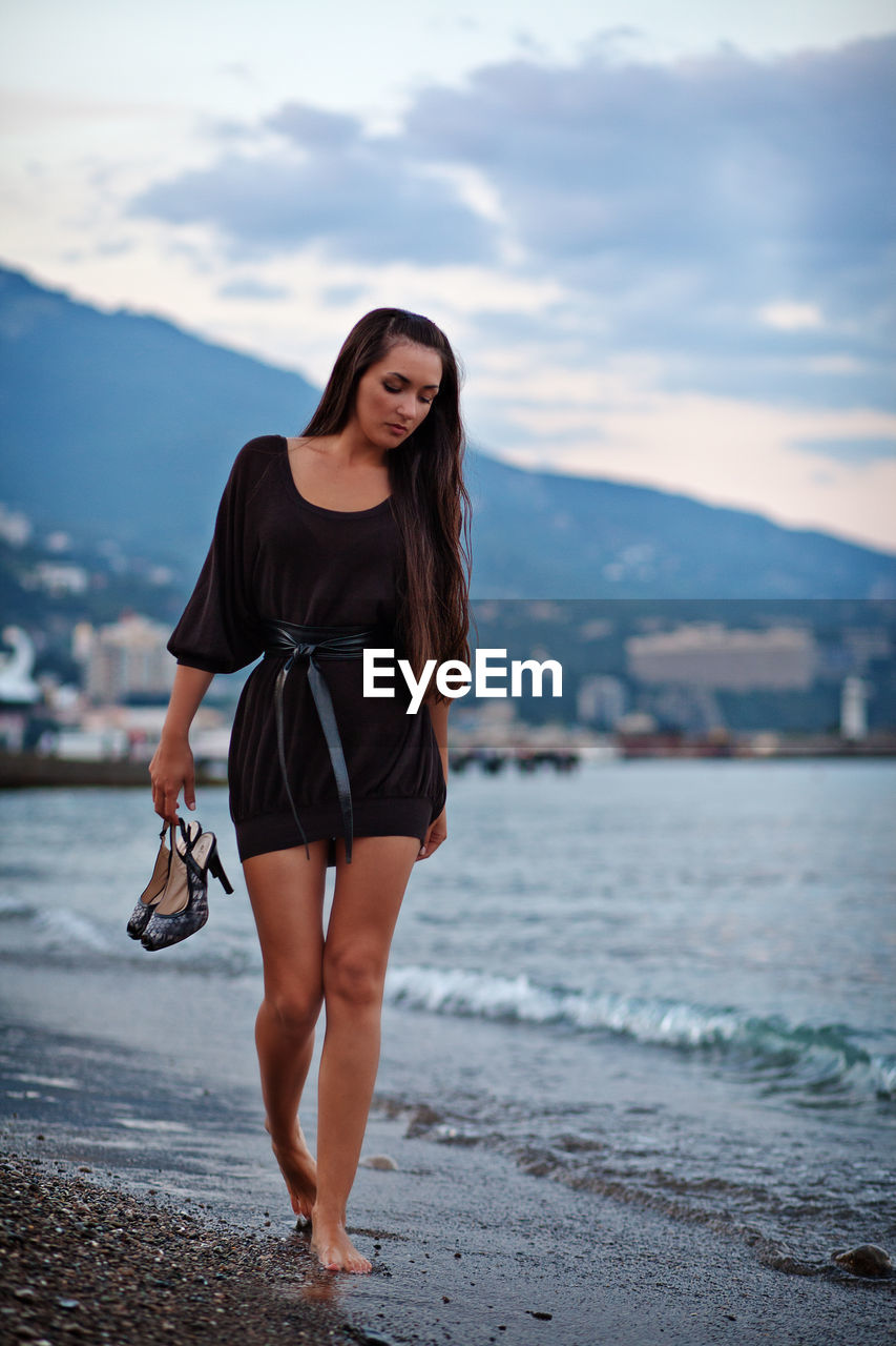 Young woman walking at beach against sky