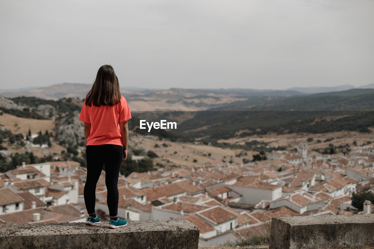 Traveler standing on stone and observing ancient ruined buildings located in highlands while visiting grazalema village in spain during vacation