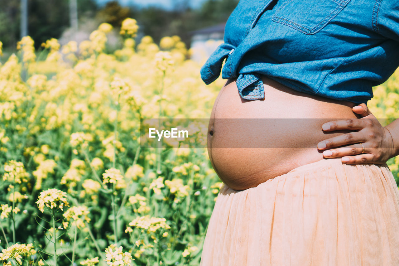 MIDSECTION OF WOMAN STANDING BY FLOWERING PLANTS