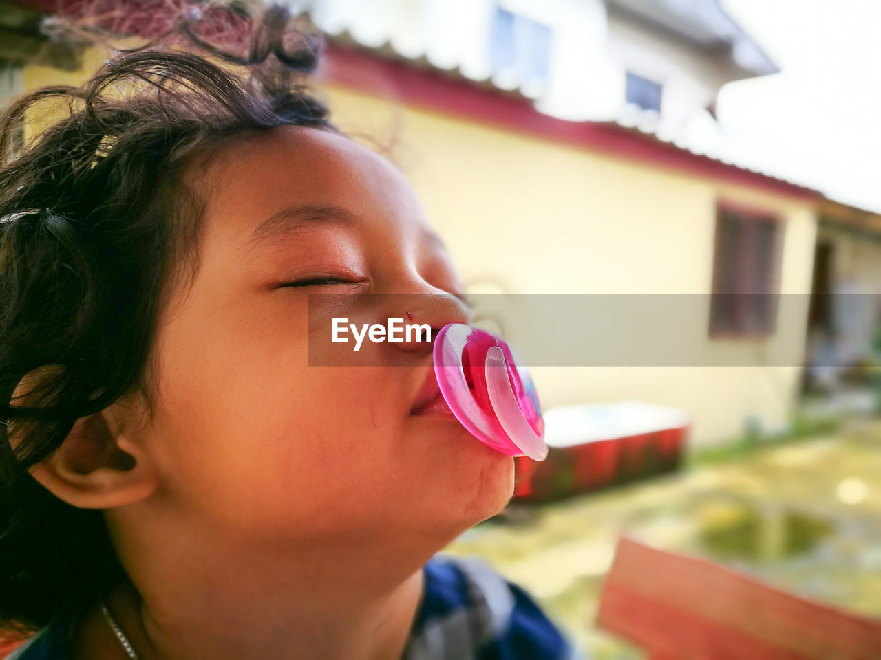 Close-up of boy with pacifier in mouth against house