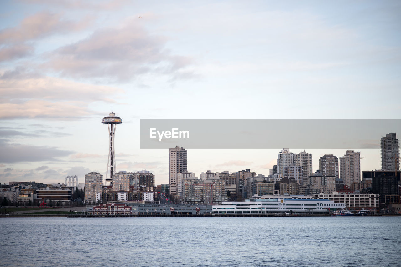 View of city at waterfront against cloudy sky