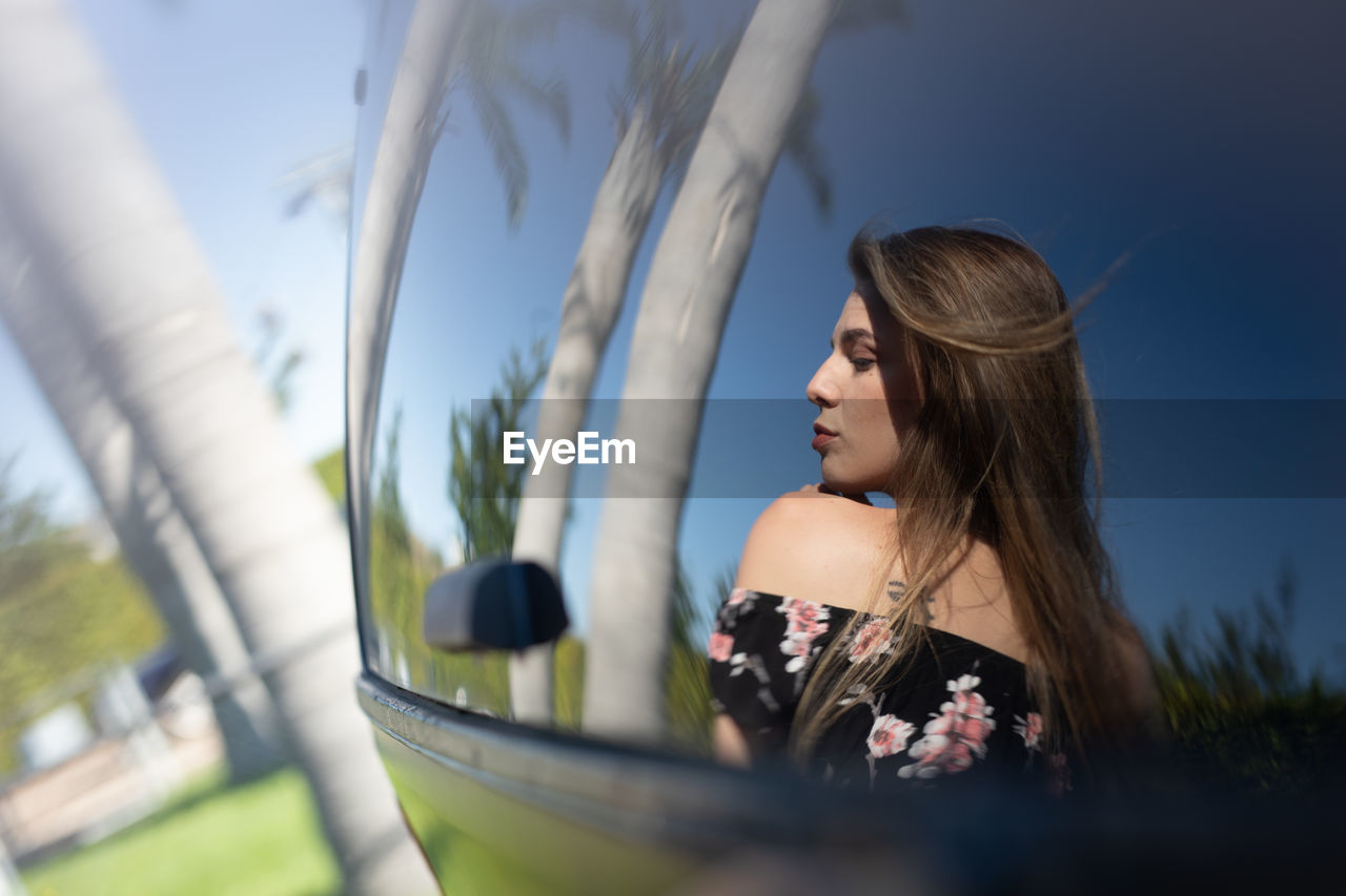 Close-up of young woman reflecting in car outdoors