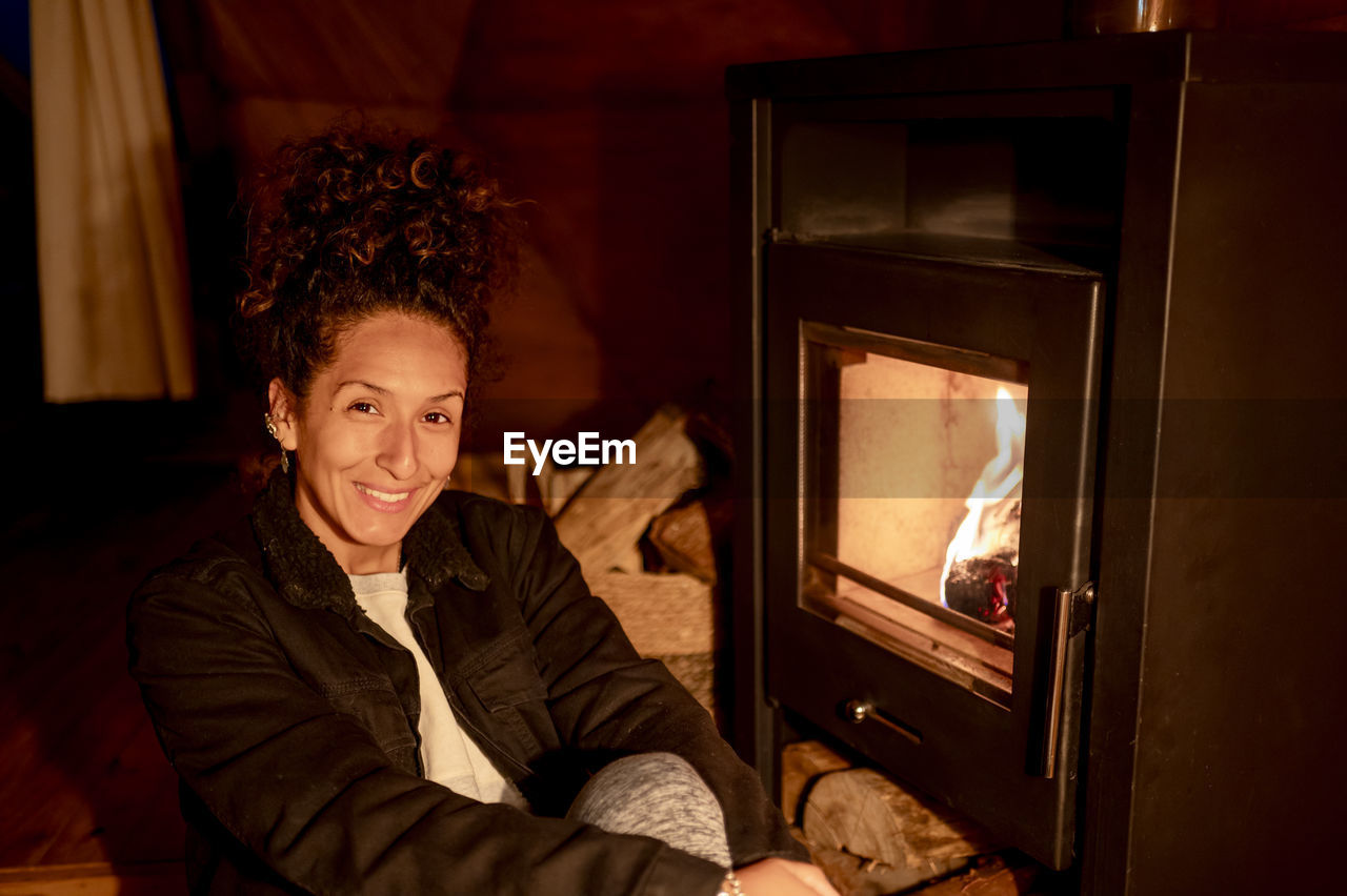 Joyful and relaxed woman sitting next to fireplace.