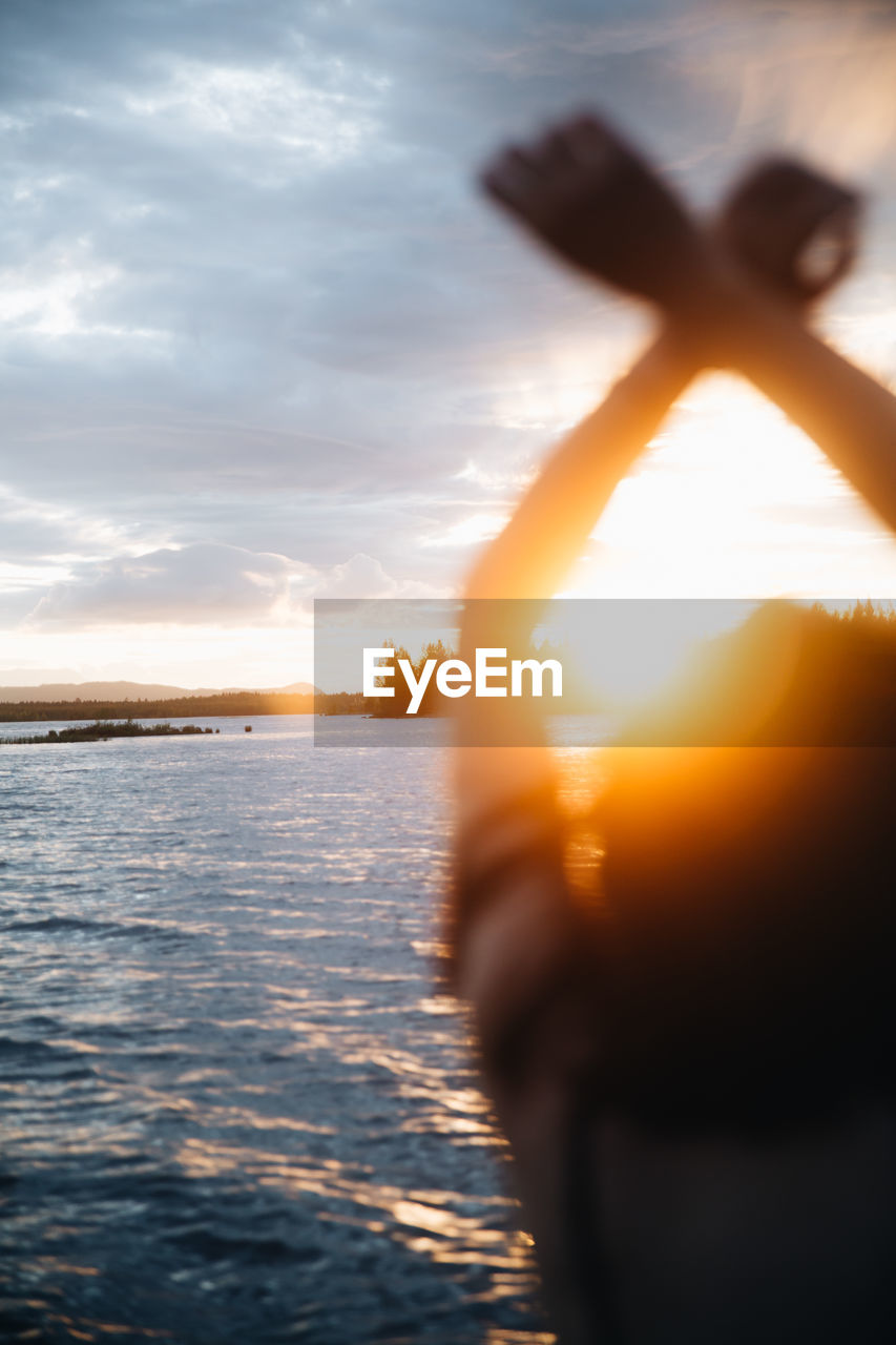 Cropped hand of woman standing at beach against sky during sunset