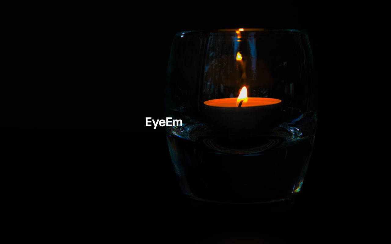 Close-up of lit candle inside a glass shot glass against black background