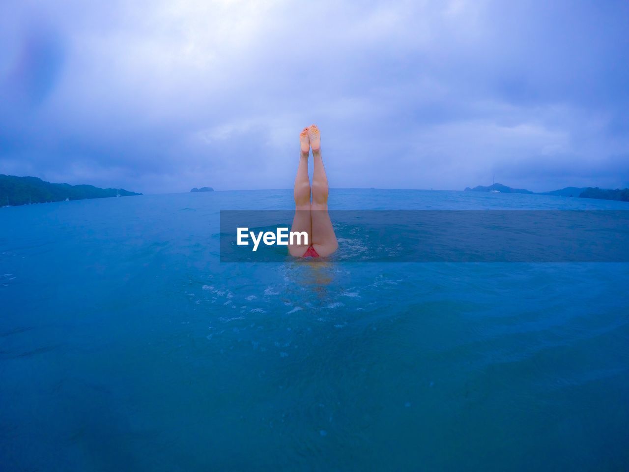 LOW SECTION OF WOMAN STANDING IN SEA AGAINST SKY