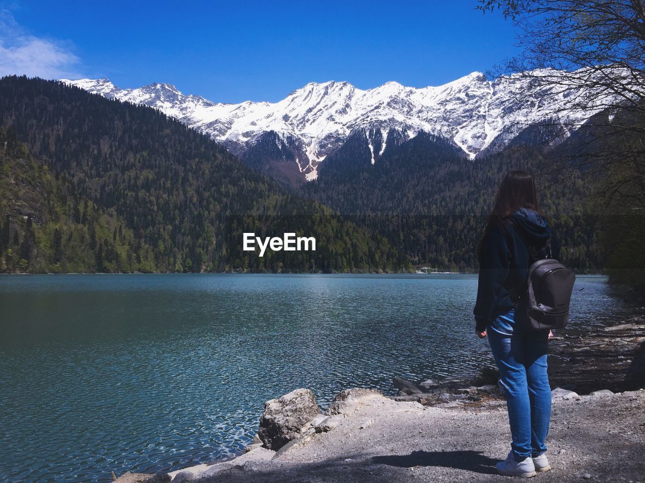 Full length of woman with backpack looking at lake by mountains during winter