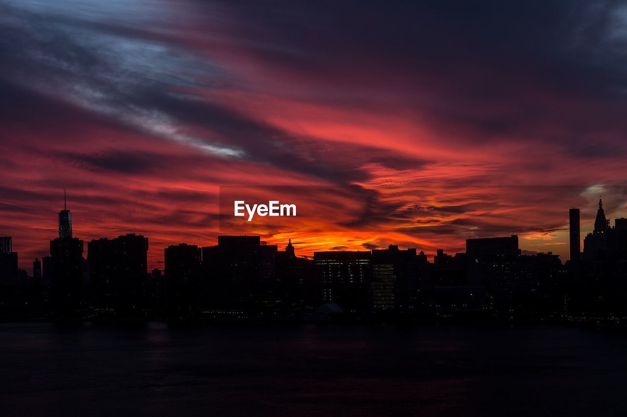 Silhouette cityscape against dramatic sky during sunset