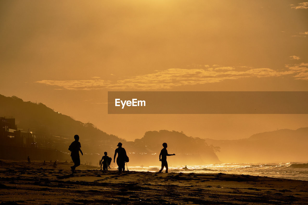 Silhouette people on beach against sky during sunrise