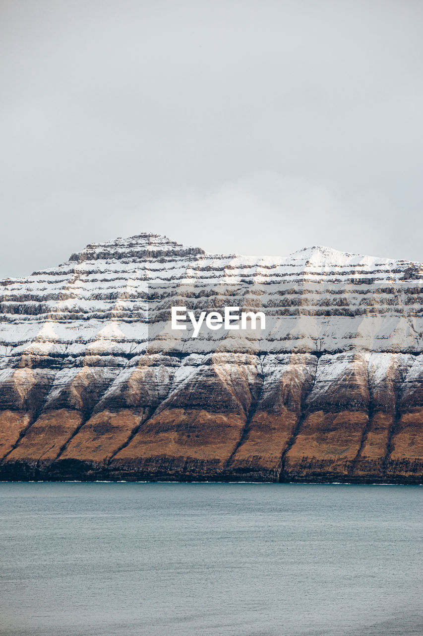 Majestic scenery of rocky terrain covered with snow near calm sea on cloudy day on faroe islands