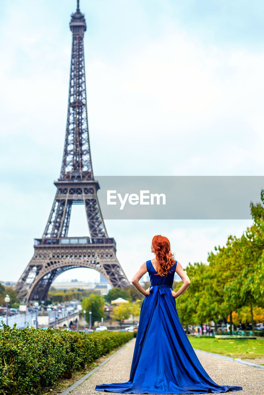 Rear view of bride in blue dress standing on footpath against eiffel tower