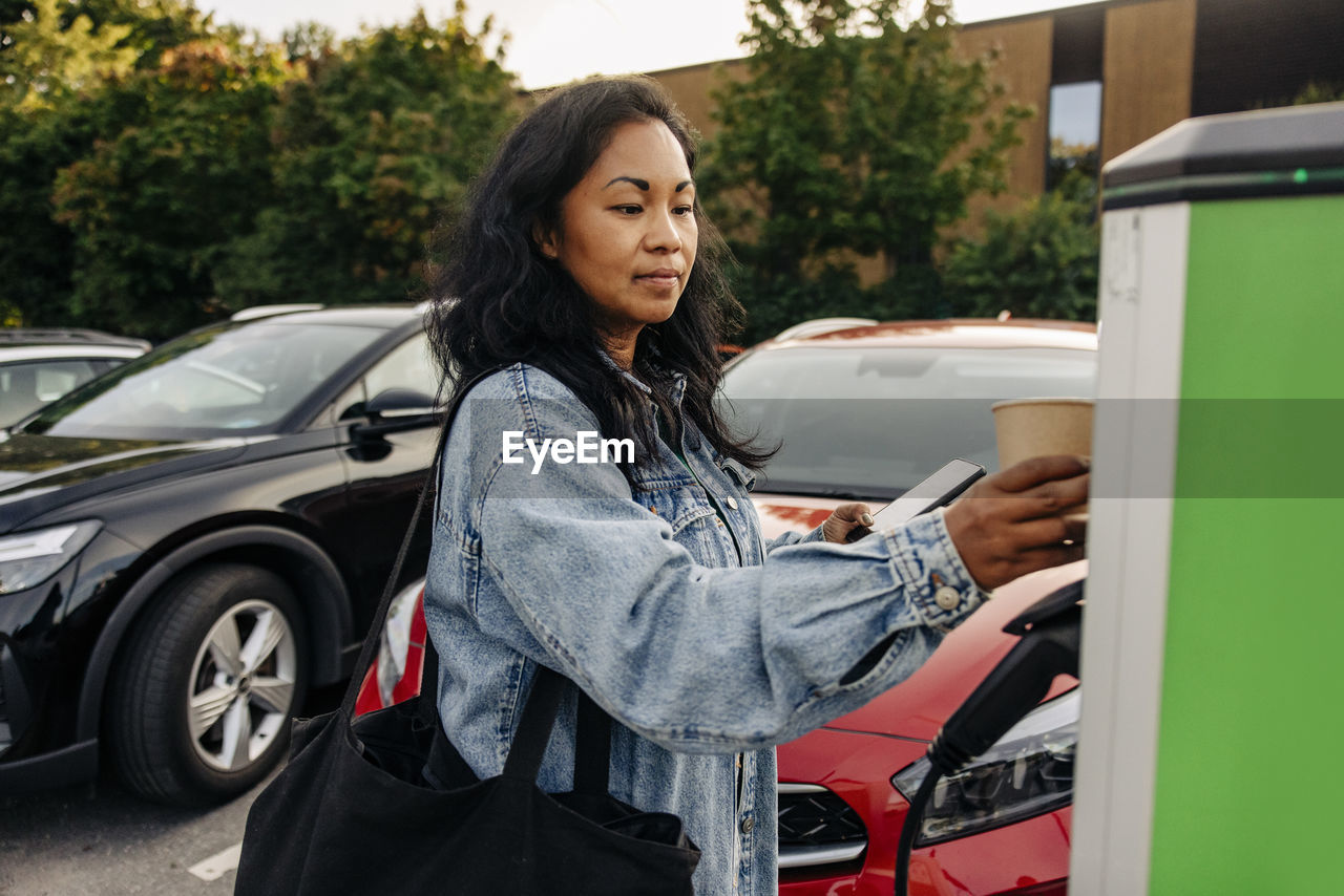 Woman wearing denim jacket operating kiosk at charging station