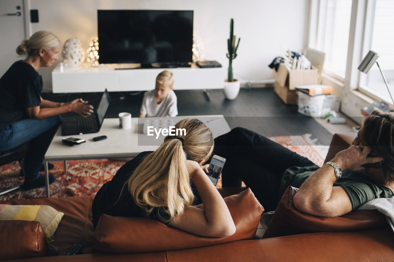 High angle view of family sitting in living room with technologies at home