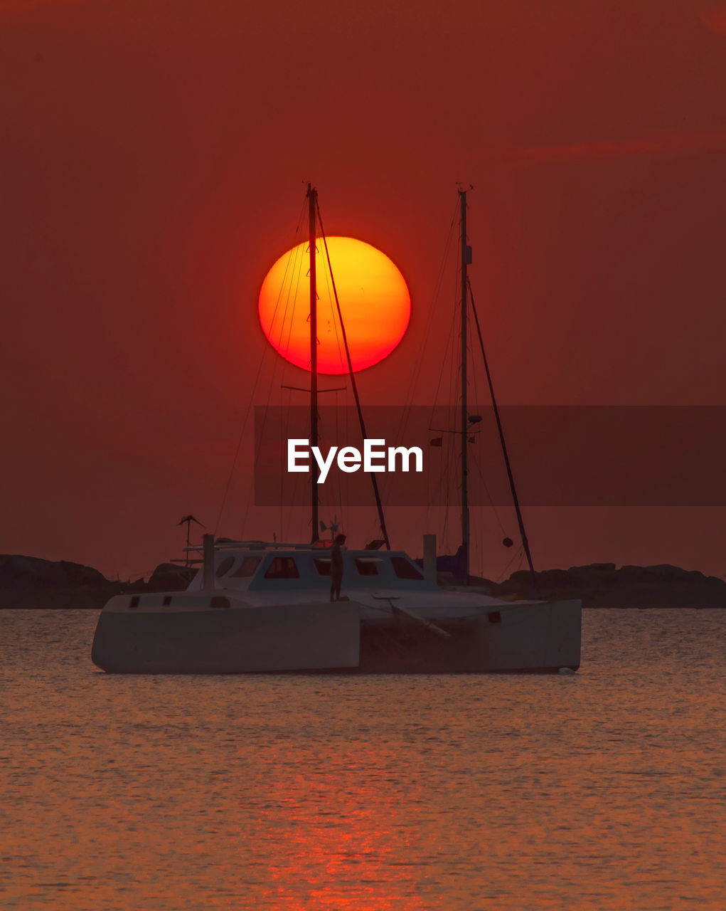 BOATS MOORED AT SEA AGAINST ORANGE SKY