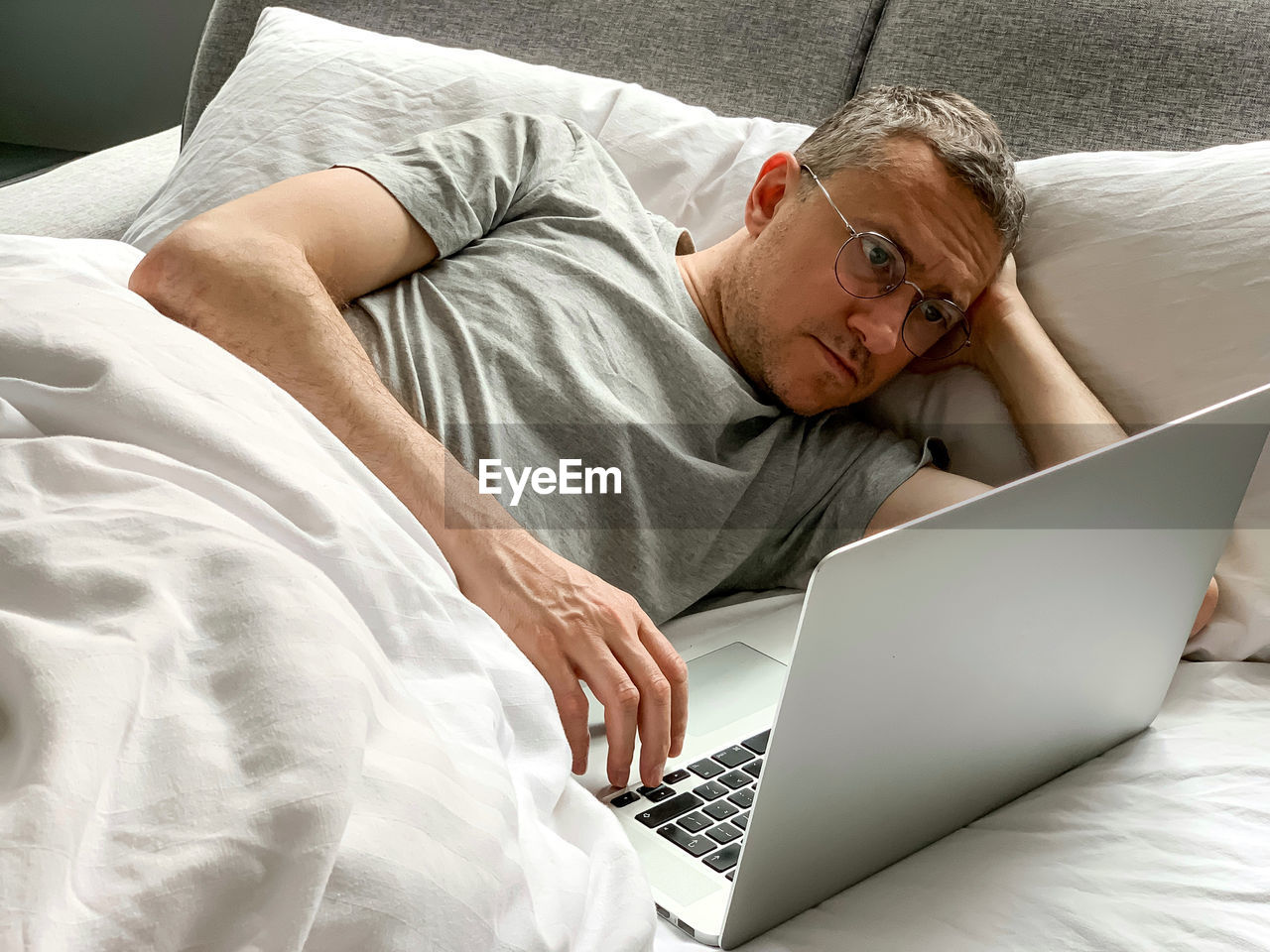 Middle aged adult man using laptop at home in bed vibes white bedsheets alone early morning working
