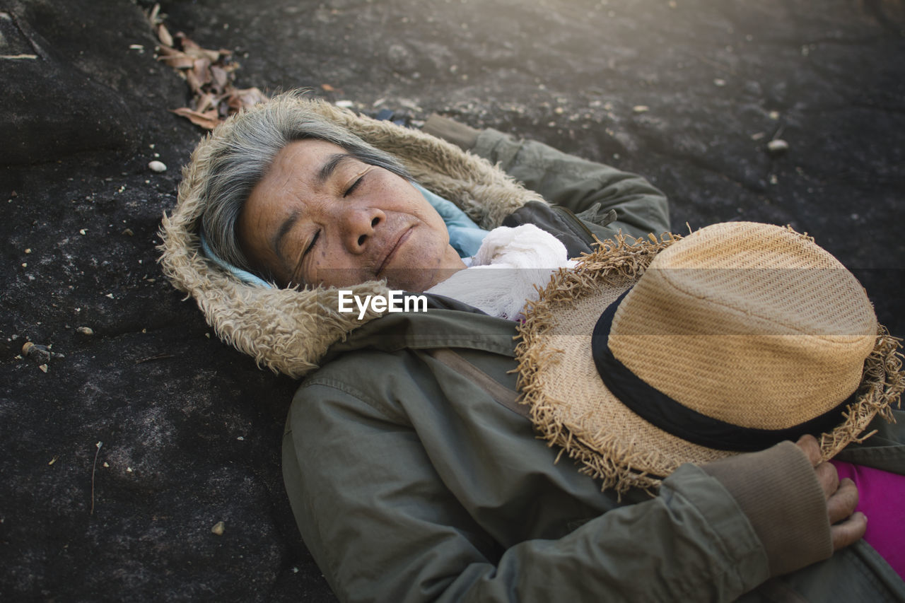 Portrait of smiling senior woman lying on rock at forest