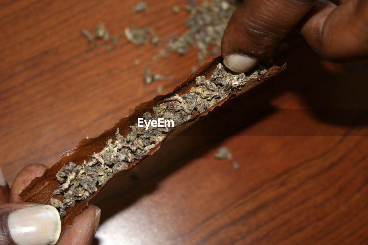 Close-up of hand making marijuana joint on table