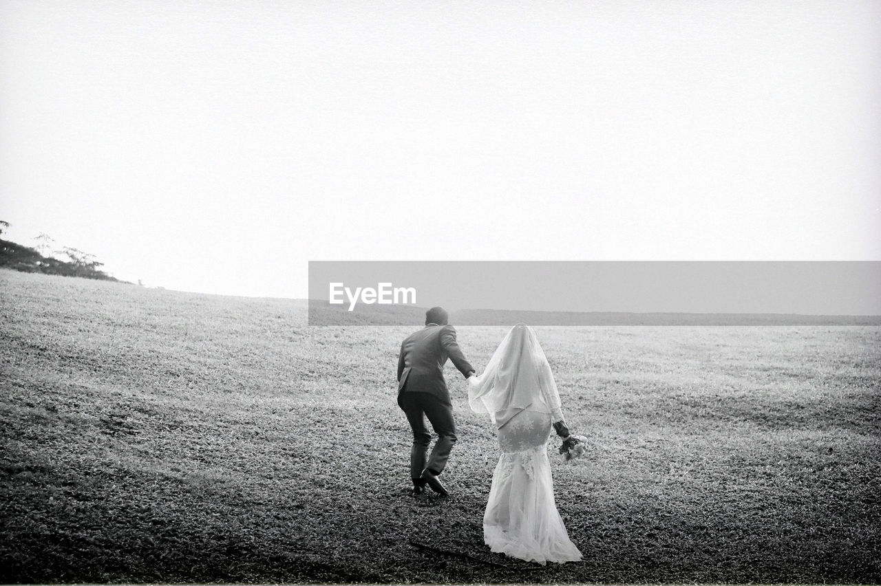 Newly married couple on field against clear sky